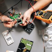Close-up of technician using multimeter to diagnose electronic circuit board, troubleshooting computer hardware, installing parts, repairing modern digital device, measuring voltage on motherboard.